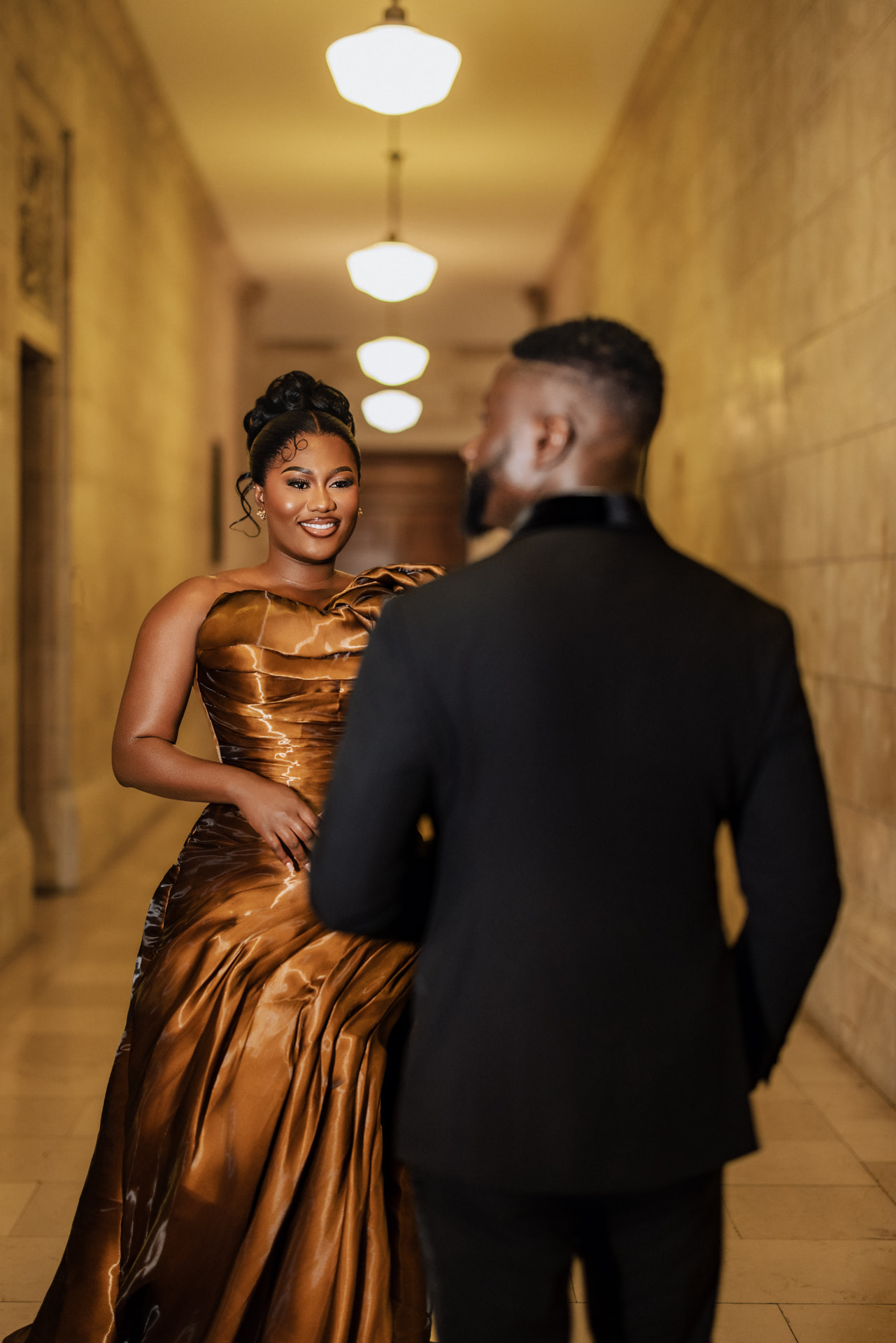Priscilla smiling at Emmanuel in the illuminated hallway